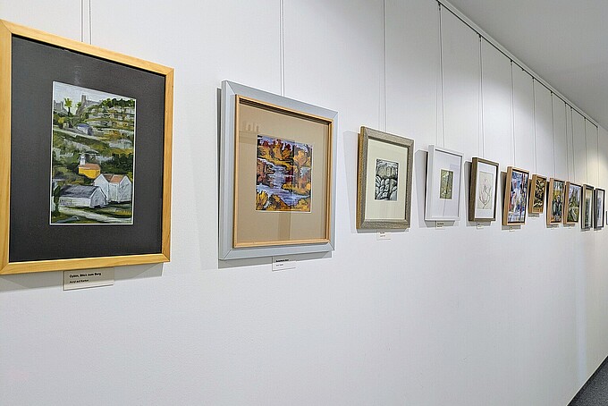 An einer weißen Wand hängen mehrfarbige Gemälde nebeneinander.