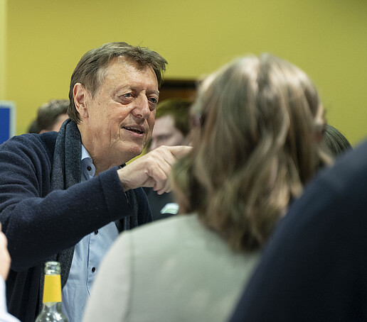 Ein Gast deutet im Gespräch auf etwas im Saal.
