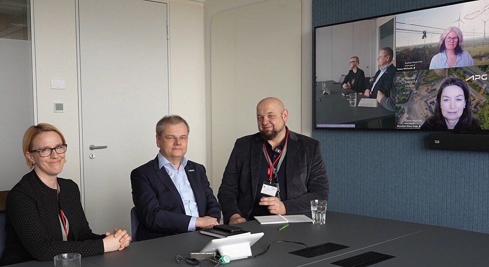 3 Personen in Präzenz am Tisch in einer Videokonferenz