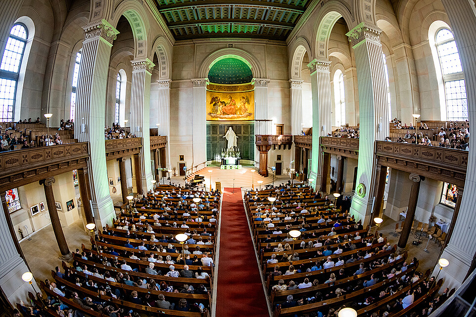 Blick von der Empore in die voll besetzte Johanniskirche Zittau mit grün beleuchtetem Altarraum und HSZG-Würfeln.