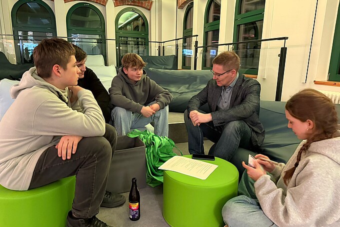 Schüler sitzen auf grünen Sitzhockern und unterhalten sich mit einem Berater.
