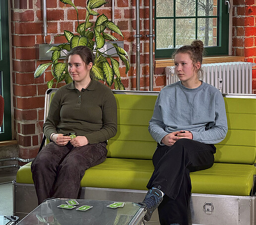 Zwei Studentinnen sitzen auf dem grünen Sofa im TV-Studio.