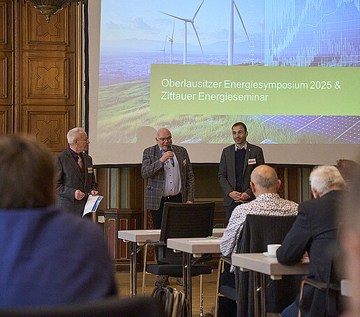 Vortragende stehen vor einer Präsentation im Zittauer Bürgersaal vor dem Publikum und halten Eröffnungsworte.