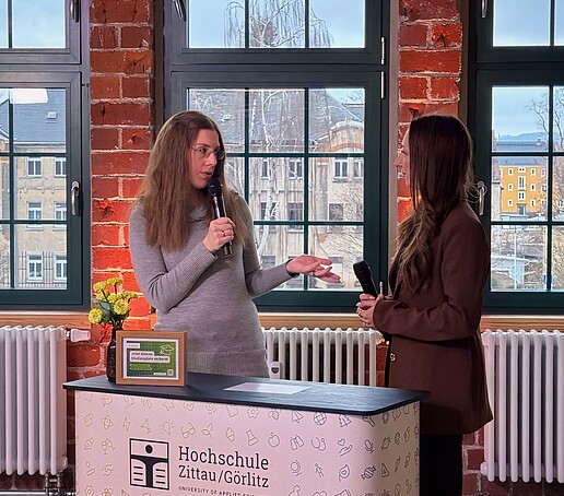 Claudia Döring wird von der Moderatorin am Messestand im TV-Studio im Celsiuz interviewt. Sie hält ein Mikrofon in der Hand.