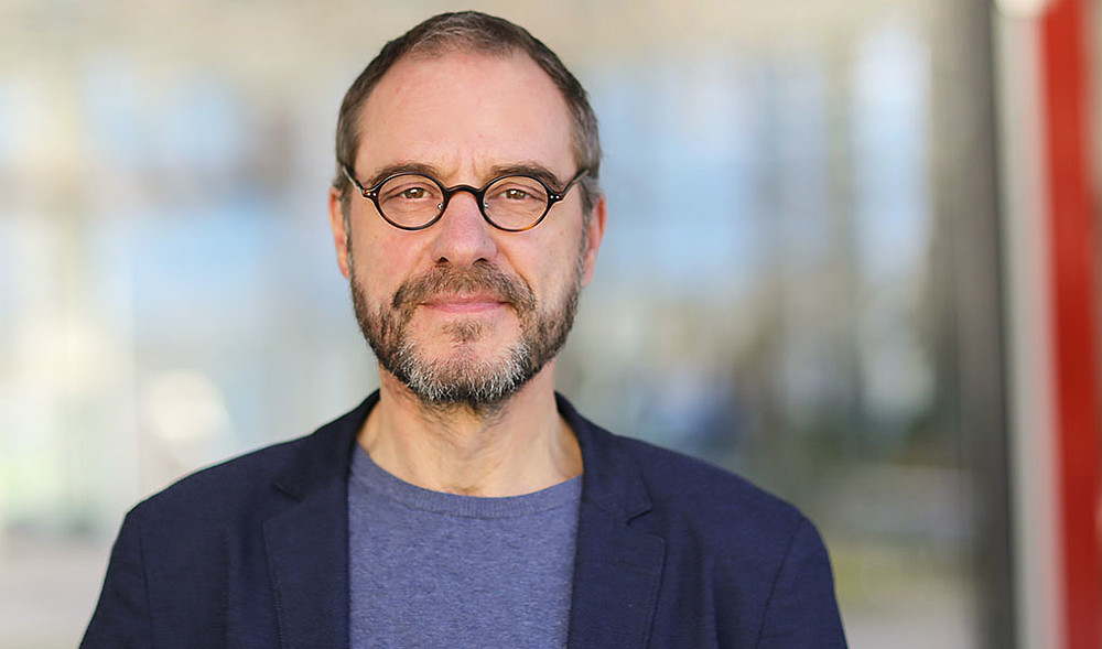 Prof. Kollmorgen im blauen Sacko und mit Brille lächelt in die Kamera.