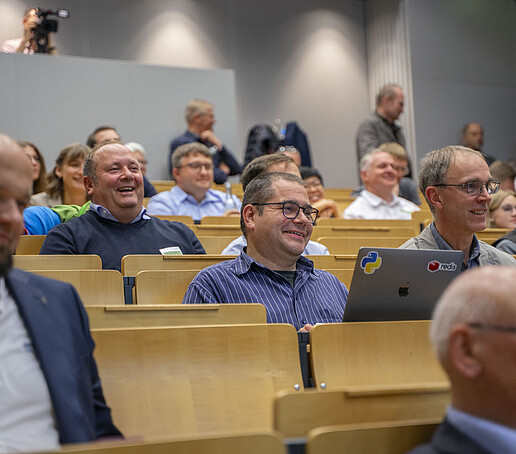 Im Publikum sitzen lächelnde und lachende Gäste.